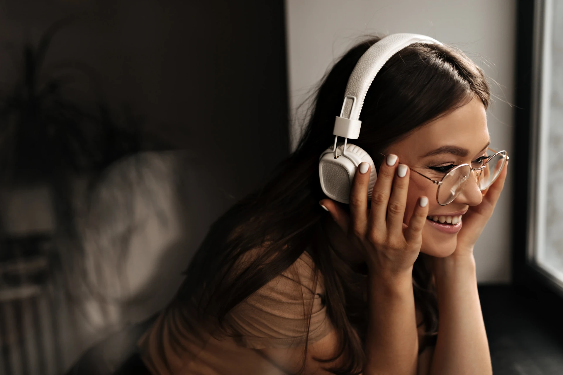 positive-woman-white-massive-headphones-puts-glasses-smiles-leaning-black-window-sill